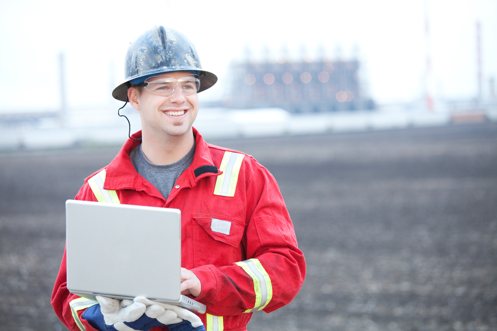 En man i hjälp och röda arbetskläder ler och håller i en laptop.jpg